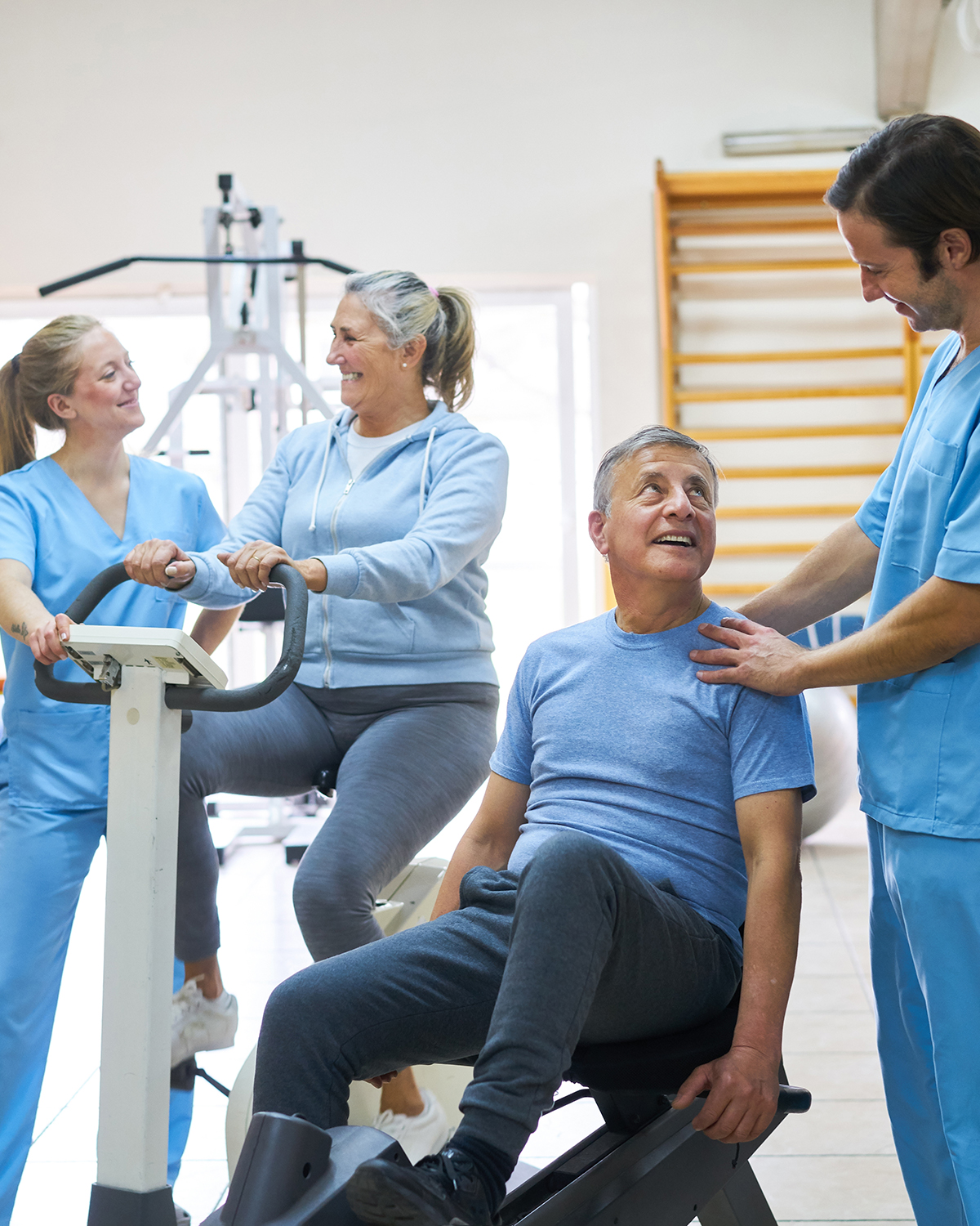 Therapists assisting happy senior man and woman exercising in rehabilitation center